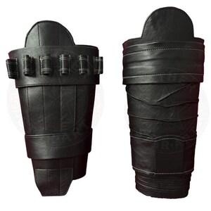May include: A pair of black leather arm guards featuring a structured design with visible white stitching. The left guard includes a row of five small cylindrical loops across the top, while the right guard displays a series of horizontal folds.