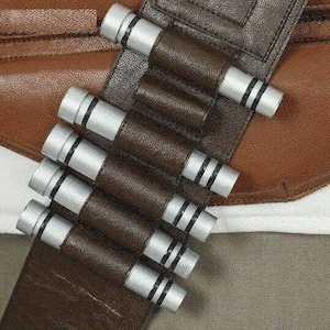 May include: Close-up of a brown leather belt with silver and black cylindrical details. The belt is attached to a brown leather garment. The design suggests a costume or cosplay accessory.