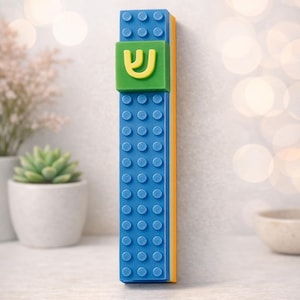 May include: A blue, yellow, and green decorative item resembling a building block. The blue section has circular studs, with a green square featuring a yellow Hebrew letter. The item is vertical, with an orange side.