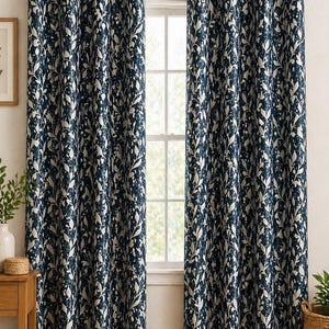 Puede incluir: Cortinas con estampado de hojas azul marino y crema colgadas de una barra plateada. Las cortinas están hechas de una tela gruesa y tienen ojales en la parte superior. Las cortinas enmarcan una ventana con luz natural.