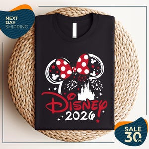 A black t-shirt with a Disney-themed design, including a pair of Mickey Mouse ears, fireworks, and the text "Disney 2020". The t-shirt is displayed on a woven placemat, and there are two sale signs indicating a 30% discount.