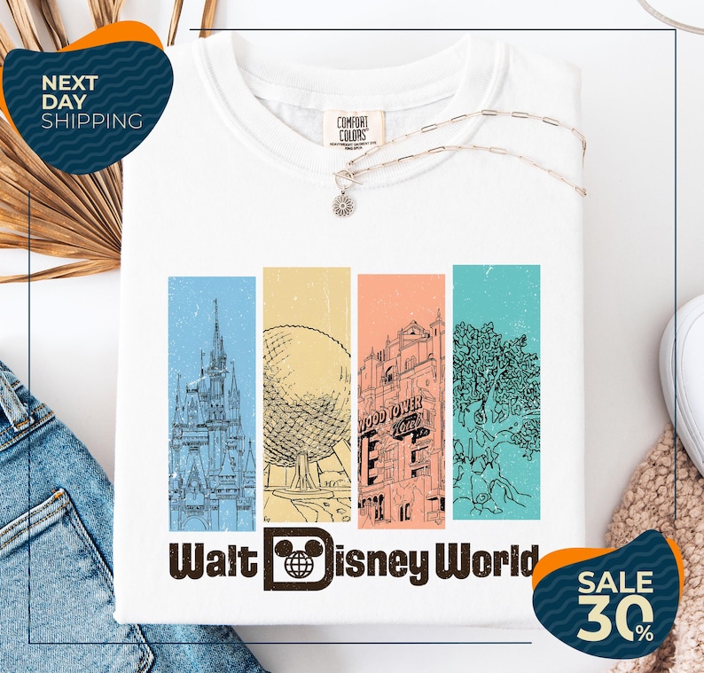 a white t-shirt with a graphic design of Disney World landmarks, including a castle, an Eiffel Tower, and a roller coaster. The t-shirt is displayed on a white background, and there are jeans and a sweater visible in the background. The image also includes text that reads "Next Day Shipping" and "SALE 30%".