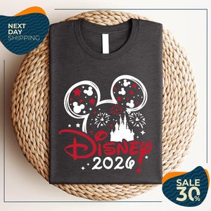 A gray t-shirt with a Disney-themed design, including Mickey Mouse ears and fireworks, is displayed on a woven placemat.