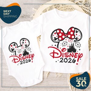 two Disney-themed t-shirts, one larger and one smaller, both with the text "Disney 2020" printed on them. The larger t-shirt is positioned on top of the smaller one, and both are placed on a wooden surface.
