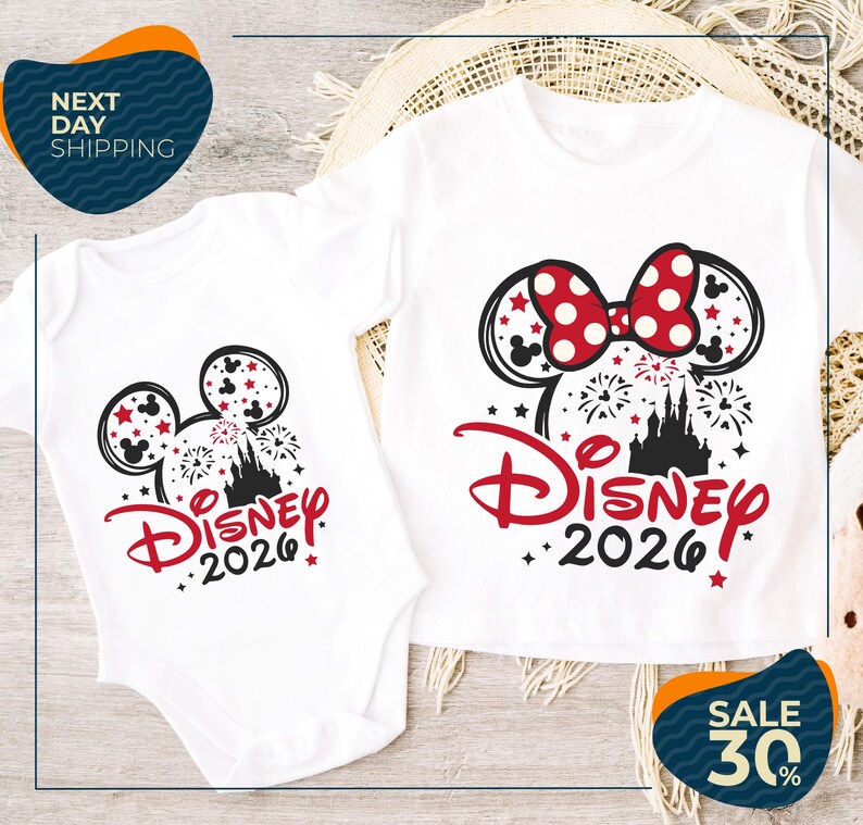 two Disney-themed t-shirts, one larger and one smaller, both with the text "Disney 2020" printed on them. The larger t-shirt is positioned on top of the smaller one, and both are placed on a wooden surface.