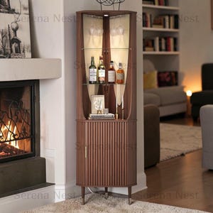May include: A tall, dark wood corner cabinet featuring a fluted door design, glass shelving, and integrated interior lighting. The upper section holds hanging stemware and liquor bottles, while the lower cabinet provides enclosed storage space.
