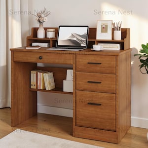 May include: A wooden desk with a hutch, featuring a central drawer, three side drawers with black handles, and open shelving. The desk surface holds a laptop, a vase with dried flowers, a candle, a framed print, and a cup with pens.
