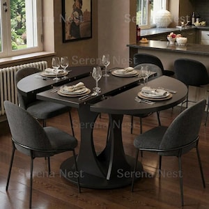 May include: A dark gray dining table with a unique design, surrounded by six matching chairs. The table is set with plates, silverware, and wine glasses. The table's base has a distinctive, sculptural shape. The chairs have dark gray fabric seats and black metal frames.