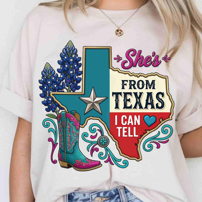 May include: A cream-colored t-shirt featuring a graphic of the state of Texas with a silver star, bluebonnet flowers, and a turquoise and pink cowboy boot. The text reads "She's FROM TEXAS I CAN TELL" with a blue heart icon and decorative swirls.