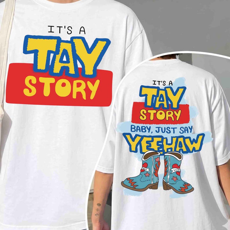 May include: A white t-shirt featuring a graphic print. The front displays the text IT'S A TAY STORY in yellow and blue letters over a red rectangle. The back shows the same text, plus BABY, JUST SAY YEEHAW and two light blue cowboy boots.