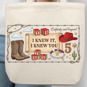 Puede incluir: Un bolso de tela color crema con un estampado gr&aacute;fico que incluye un pergamino con el texto I KNEW IT, I KNEW YOU, rodeado de botas vaqueras, un sombrero rojo, bloques de letras con TS5, una pulsera de cuentas, un cactus y estrellas.