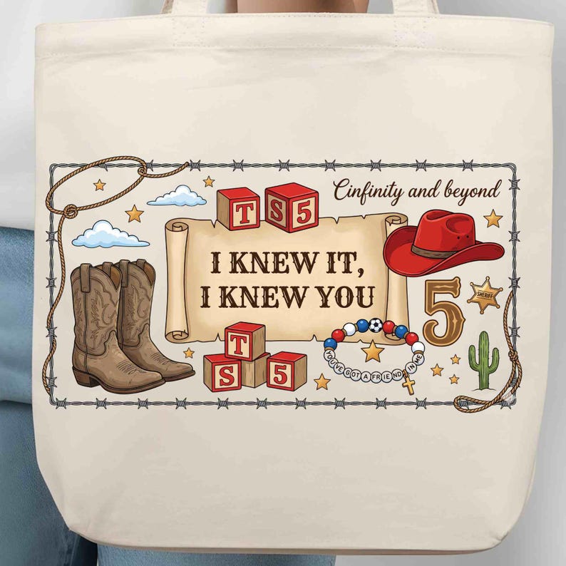 Puede incluir: Un bolso de tela color crema con un estampado gr&aacute;fico que incluye un pergamino con el texto I KNEW IT, I KNEW YOU, rodeado de botas vaqueras, un sombrero rojo, bloques de letras con TS5, una pulsera de cuentas, un cactus y estrellas.