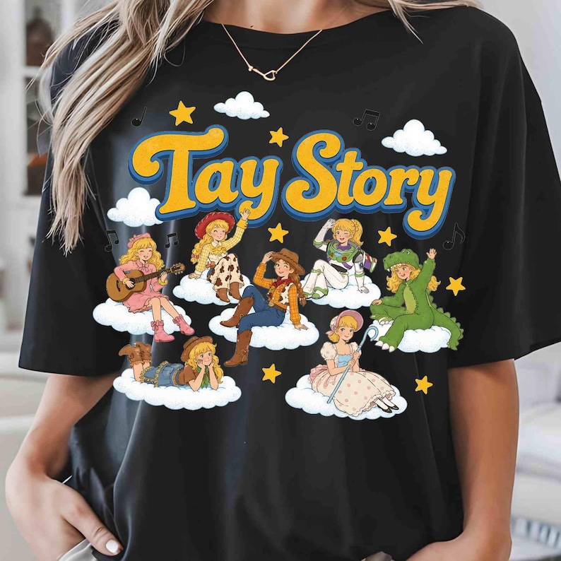 Puede incluir: Una camiseta negra con el texto amarillo Tay Story y un estampado gr&aacute;fico de varios personajes rubios vestidos con diversos disfraces, cada uno sentado sobre una nube blanca rodeado de estrellas amarillas y peque&ntilde;as notas musicales negras.