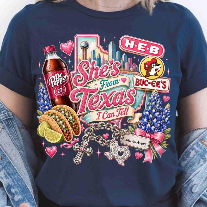 May include: A navy blue t-shirt featuring a graphic print with the text She's From Texas I Can Tell. The design includes a Dr Pepper bottle, tacos with lime wedges, a city skyline, H-E-B and Buc-ee's logos, bluebonnets, and a charm bracelet with a cross.