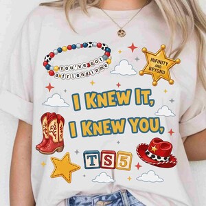 May include: A white t-shirt featuring a graphic print with a beaded bracelet reading 'You've got a friend in me', a gold sheriff star badge with 'INFINITY AND BEYOND', red cowboy boots, a red cowboy hat, and blocks spelling 'TS5'. Text reads 'I KNEW IT, I KNEW YOU'.