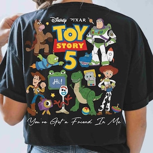May include: A black t-shirt featuring a colorful graphic of Disney Pixar Toy Story characters including Woody, Buzz Lightyear, Jessie, Rex, and Forky. The design includes the text Toy Story 5, a green board with the word Hi, and You've Got a Friend In Me.