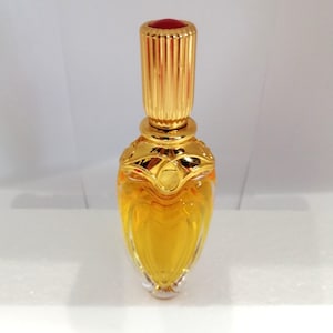 May include: A glass perfume bottle with a golden, ornate collar and a tall, ribbed golden cap topped with a small red circular accent. The bottle contains a vibrant amber-colored liquid and features a teardrop-shaped body with clear glass.