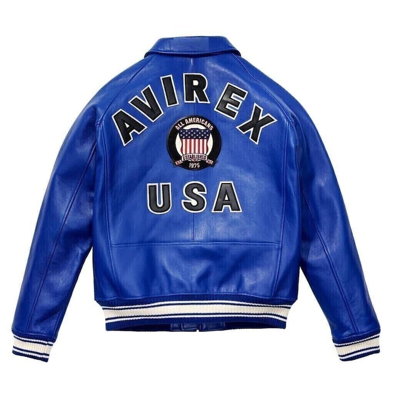 K&ouml;nnte beinhalten: Eine leuchtend blaue Lederjacke mit dem Schriftzug AVIREX in gro&szlig;en schwarzen Buchstaben auf dem oberen R&uuml;cken. Unter dem Text befindet sich ein kreisf&ouml;rmiges Abzeichen mit einem amerikanischen Flaggendesign und den Worten ALL AMERICANS ESTABLISHED 1975. Das Wort USA ist darunter in Schwarz gedruckt. Die Jacke hat einen gerippten Kragen, B&uuml;ndchen und Saum mit wei&szlig;en und blauen Streifen.