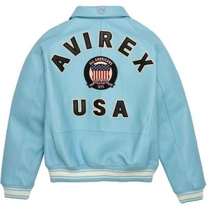 K&ouml;nnte beinhalten: Eine hellblaue Collegejacke mit dem Schriftzug AVIREX und USA in schwarzen Buchstaben auf der R&uuml;ckseite. Ein kreisf&ouml;rmiger Aufn&auml;her in der Mitte zeigt den Text ALL AMERICANS ESTABLISHED 1975 mit einer Grafik der US-Flagge. Die Jacke hat Rippb&uuml;ndchen.