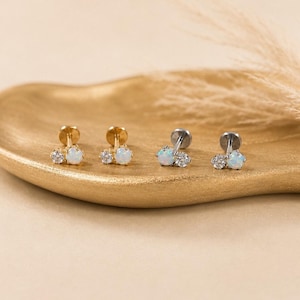May include: Two pairs of stud earrings, one pair in gold-tone metal and one pair in silver-tone metal. Each earring features a small round clear stone paired with a slightly larger round iridescent opal stone, both set in a prong setting.