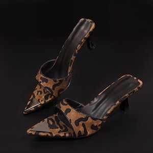 May include: A pair of open-toe mules with a pointed toe and a small heel. The shoes feature a brown and black leopard print pattern on the upper and a metallic silver accent on the toe. The heels are black.