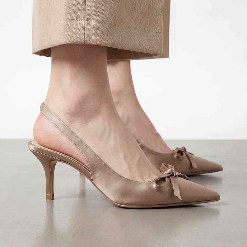 May include: Satin slingback heels in a neutral beige color. The pointed-toe shoes feature a small bow detail on the vamp and a thin strap around the heel. The heels are approximately 3 inches high.