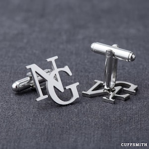 Op de afbeelding: Zilveren manchetknopen met de initialen "NG" in een gestileerd lettertype. De manchetknopen worden gepresenteerd op een grijze, getextureerde achtergrond. Het woord "CUFFSMITH" staat rechtsonder in het wit gedrukt.