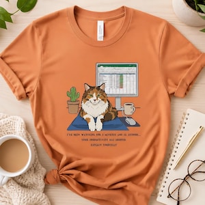 May include: Orange t-shirt featuring a cartoon cat sitting in front of a computer monitor. The cat is brown, white, and orange. Text on the shirt reads: "I'VE BEEN WATCHING FOR 3 MINUTES AND 12 SECONDS... YOUR PRODUCTIVITY HAS DROPPED. EXPLAIN YOURSELF!"