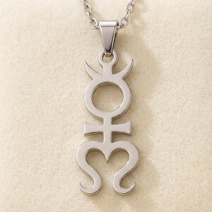 May include: A silver-toned metal pendant necklace featuring a vertical, symmetrical symbol with a circular top, a horizontal crossbar, and a stylized heart-shaped base with curved ends, suspended from a matching silver-toned link chain.
