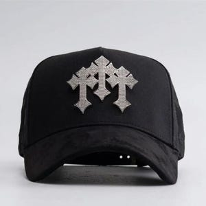 Puede incluir: Gorra de béisbol negra con un diseño de cruz plateada. La gorra tiene una visera curva y una corona estructurada. El diseño de la cruz está hecho de pequeños adornos brillantes.
