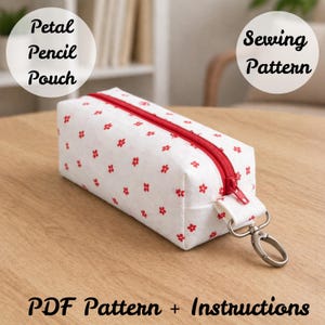 May include: A white pencil pouch with a red zipper and red floral pattern. The pouch has a silver clasp and a white strap. Text on the image reads "Petal Pencil Pouch", "Sewing Pattern", and "PDF Pattern + Instructions".
