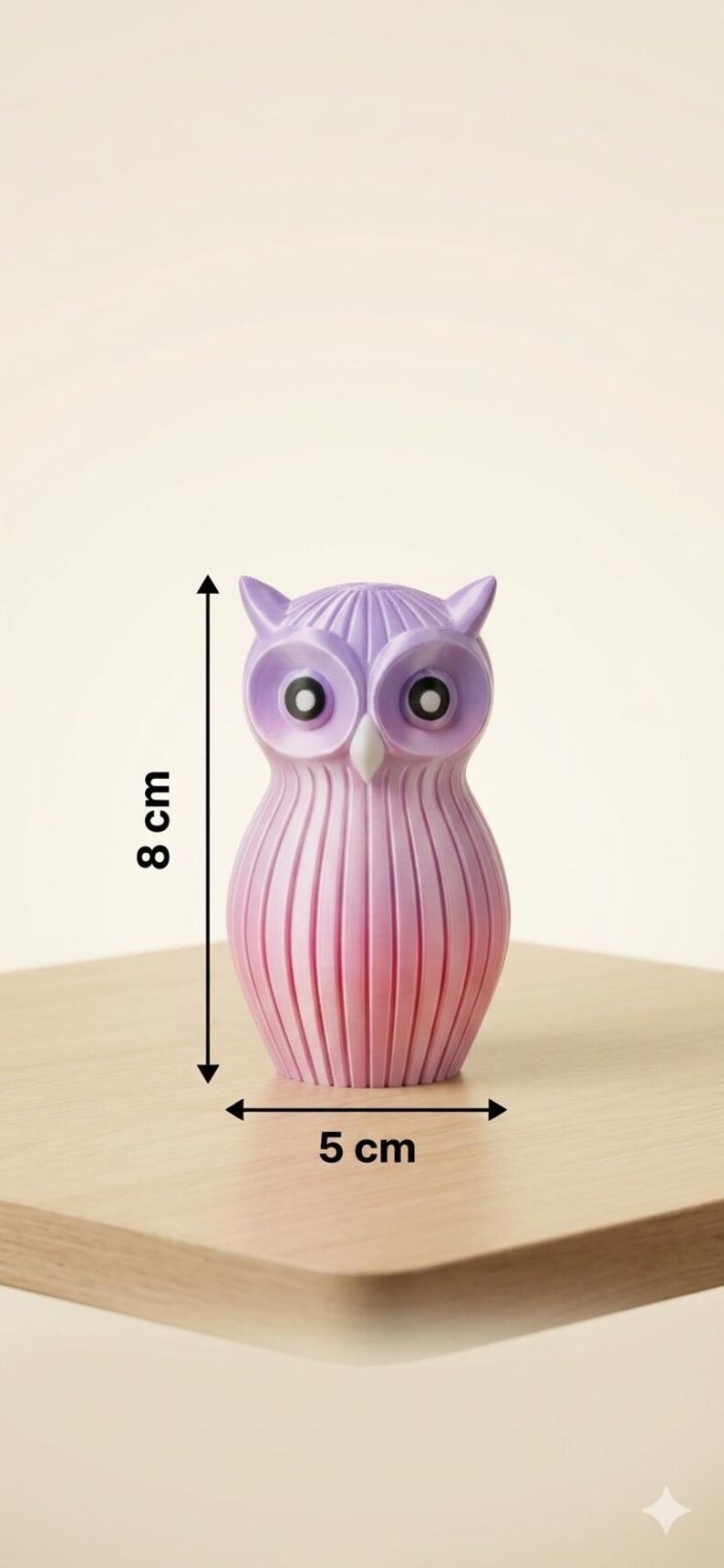 Puede incluir: Una figura decorativa de b&uacute;ho, de aproximadamente 5 cm de ancho y 8 cm de alto, en tonos rosas y morados. El b&uacute;ho tiene ojos grandes y un cuerpo texturizado y acanalado. Se exhibe sobre una superficie de madera.