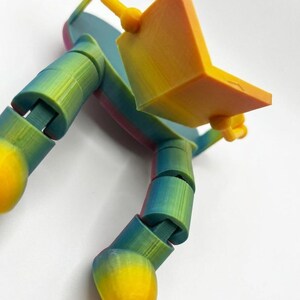May include: A multi-coloured 3D-printed articulated finger toy. The toy features a gradient of colours, including yellow, orange, green, and blue. It is designed to resemble a finger with a small laptop attached, with flexible joints.