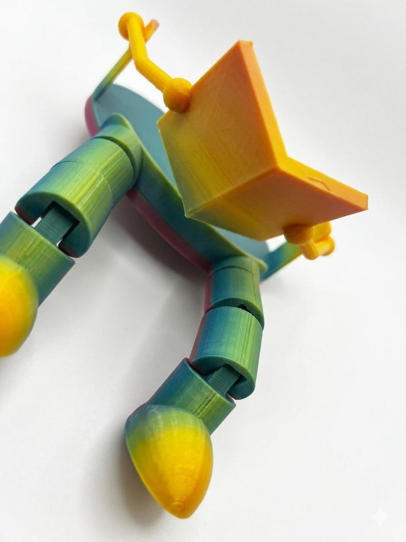 May include: A multi-coloured 3D-printed articulated finger toy. The toy features a gradient of colours, including yellow, orange, green, and blue. It is designed to resemble a finger with a small laptop attached, with flexible joints.