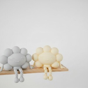 K&ouml;nnte beinhalten: Zwei skurrile, wolkenf&ouml;rmige Figuren in Hellgrau und Creme, jeweils mit einem l&auml;chelnden Gesicht und h&auml;ngenden Beinen, sitzen auf einem kleinen Holzregal. Die Figuren haben ein verspieltes Design, perfekt f&uuml;r die Kinderzimmerdekoration.