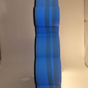 Puede incluir: Un jarr&oacute;n decorativo azul, alto y con un dise&ntilde;o &uacute;nico en capas. El jarr&oacute;n tiene forma cil&iacute;ndrica con secciones redondeadas apiladas. Rayas verticales de color azul claro crean un patr&oacute;n a rayas. El jarr&oacute;n mide unos 30 cm de altura.