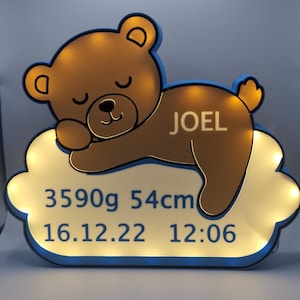 Puede incluir: Una luz de noche con forma de oso de peluche marr&oacute;n con el nombre "JOEL" en una base con forma de nube. La base muestra el peso al nacer del beb&eacute; de 3590g, la longitud de 54cm y la fecha y hora de nacimiento: 16.12.22 12:06.
