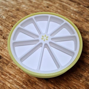 以下が含まれることがあります： 白と黄色のプラスチック製のレモン型トレイで、セグメント化されたコンパートメントがあります。トレイには黄色の縁と中央に小さな花の模様があります。トレイはレモンスライスに似せてデザインされています。