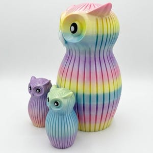 Puede incluir: Tres figuras de b&uacute;hos coloridos en tonos pastel arco&iacute;ris. El b&uacute;ho m&aacute;s grande es alto y rayado, con los b&uacute;hos m&aacute;s peque&ntilde;os en tonos de morado y azul. Los b&uacute;hos tienen ojos grandes y redondos y un acabado liso y brillante.