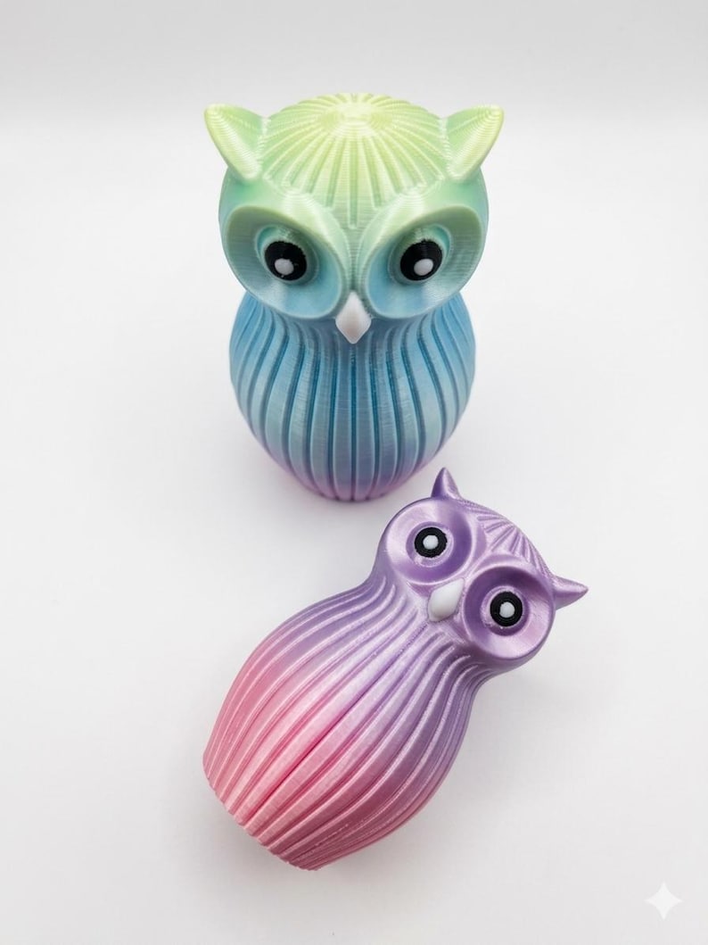Puede incluir: Dos figuras decorativas de b&uacute;ho. El b&uacute;ho m&aacute;s grande es un degradado de verde, azul y morado. El b&uacute;ho m&aacute;s peque&ntilde;o es un degradado de morado y rosa. Ambos tienen ojos negros y picos blancos.
