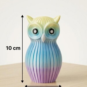 Puede incluir: Figura de b&uacute;ho colorida, de aproximadamente 5 cm de ancho y 10 cm de alto, con un degradado de amarillo, azul y morado. El b&uacute;ho tiene ojos grandes y negros y est&aacute; hecho de un material acanalado. Un art&iacute;culo decorativo.