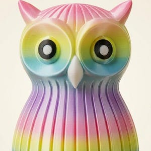 Puede incluir: Figura de b&uacute;ho multicolor con un degradado de rosa, amarillo, azul y morado. El b&uacute;ho tiene ojos grandes y redondos y un pico blanco. La figura est&aacute; hecha de un material acanalado.