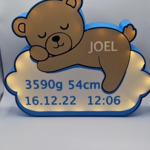 Puede incluir: Una luz de noche con forma de oso de peluche marr&oacute;n con el nombre "JOEL" en un lateral, sobre una base en forma de nube. La base muestra el peso del beb&eacute; (3590g), la longitud (54cm) y la fecha y hora de nacimiento: 16.12.22 12:06. Borde azul.