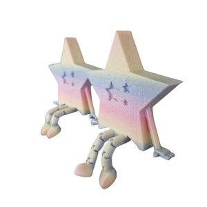 May include: Two star-shaped figurines with pastel rainbow gradients. Each star has articulated legs and arms, with a small star cutout. The color palette includes pink, blue, and yellow, creating a whimsical and playful aesthetic.