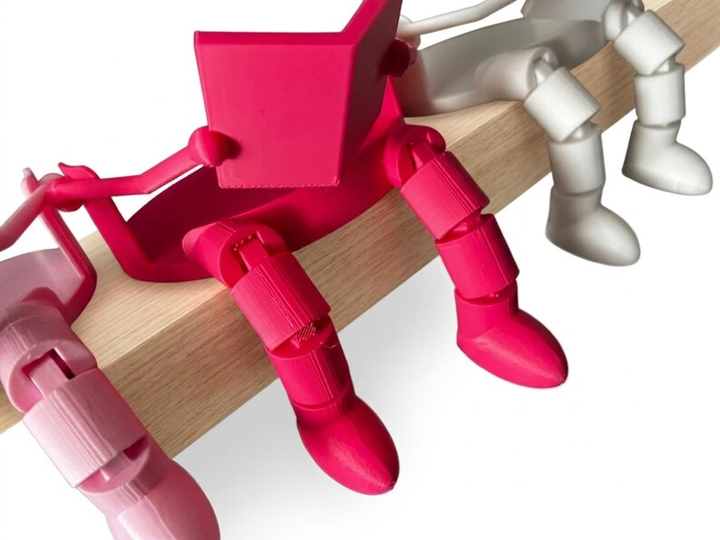 May include: A row of articulated figures in various colours, sitting on a wooden beam. The figures are reading books. The first figure is bright pink, the second is light pink, and the third is white. The figures have segmented limbs.