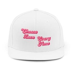 May include: White baseball cap with the text "Choose Love Every Time" in pink, retro-style lettering. The cap has a flat brim and a classic snapback closure.