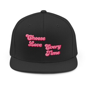 May include: Black flat-brimmed baseball cap with the phrase "Choose Love Every Time" embroidered in pink and light pink. The cap has a structured fit and a classic, casual style.
