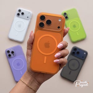 Könnte beinhalten: Eine Sammlung von fünf durchscheinenden Smartphone-Hüllen mit einem kreisförmigen magnetischen Ladering und einem quadratischen Kameraausschnitt. Die Hüllen sind in Orange, Weiß, Limettengrün, Lavendel und Dunkelgrau erhältlich, jeweils mit Apple-Logo.