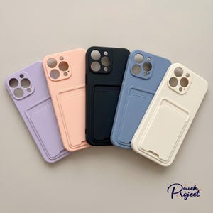 May include: Five pastel-coloured phone cases in lavender, peach, black, blue, and cream. Each case features a cardholder and camera cutouts. The cases are displayed on a light grey surface.
