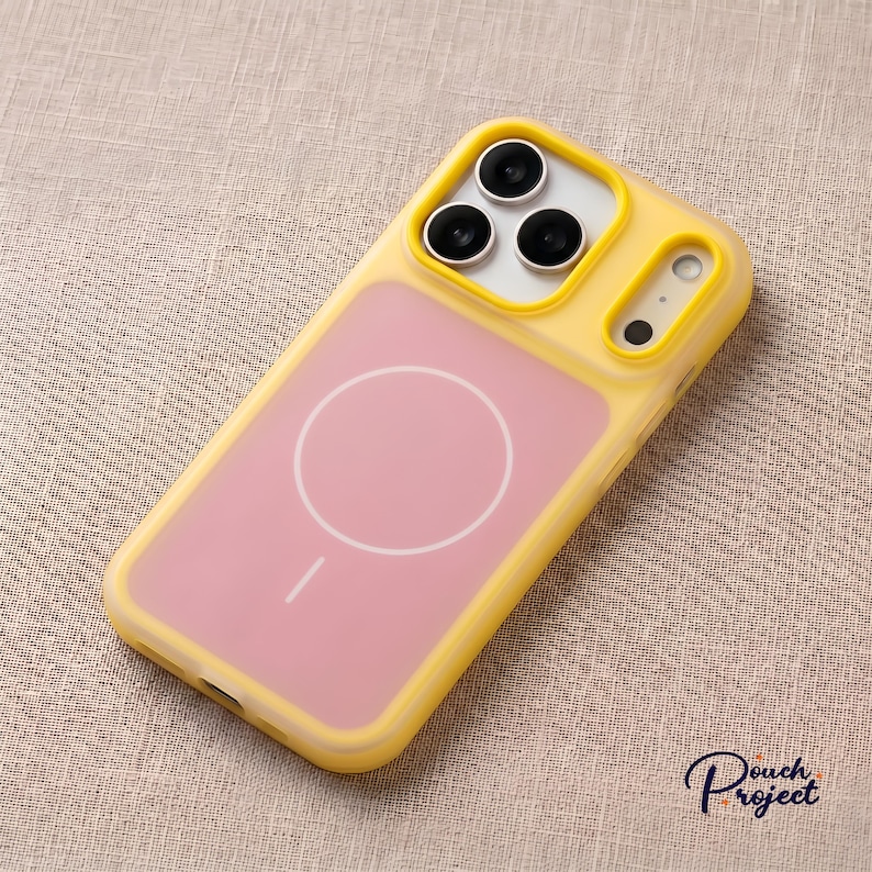 Pu&ograve; includere: Custodia per telefono gialla e rosa con design MagSafe. La custodia ha una cornice gialla e un retro rosa con un cerchio bianco e una linea. L'area della fotocamera ha tre lenti nere e un flash.